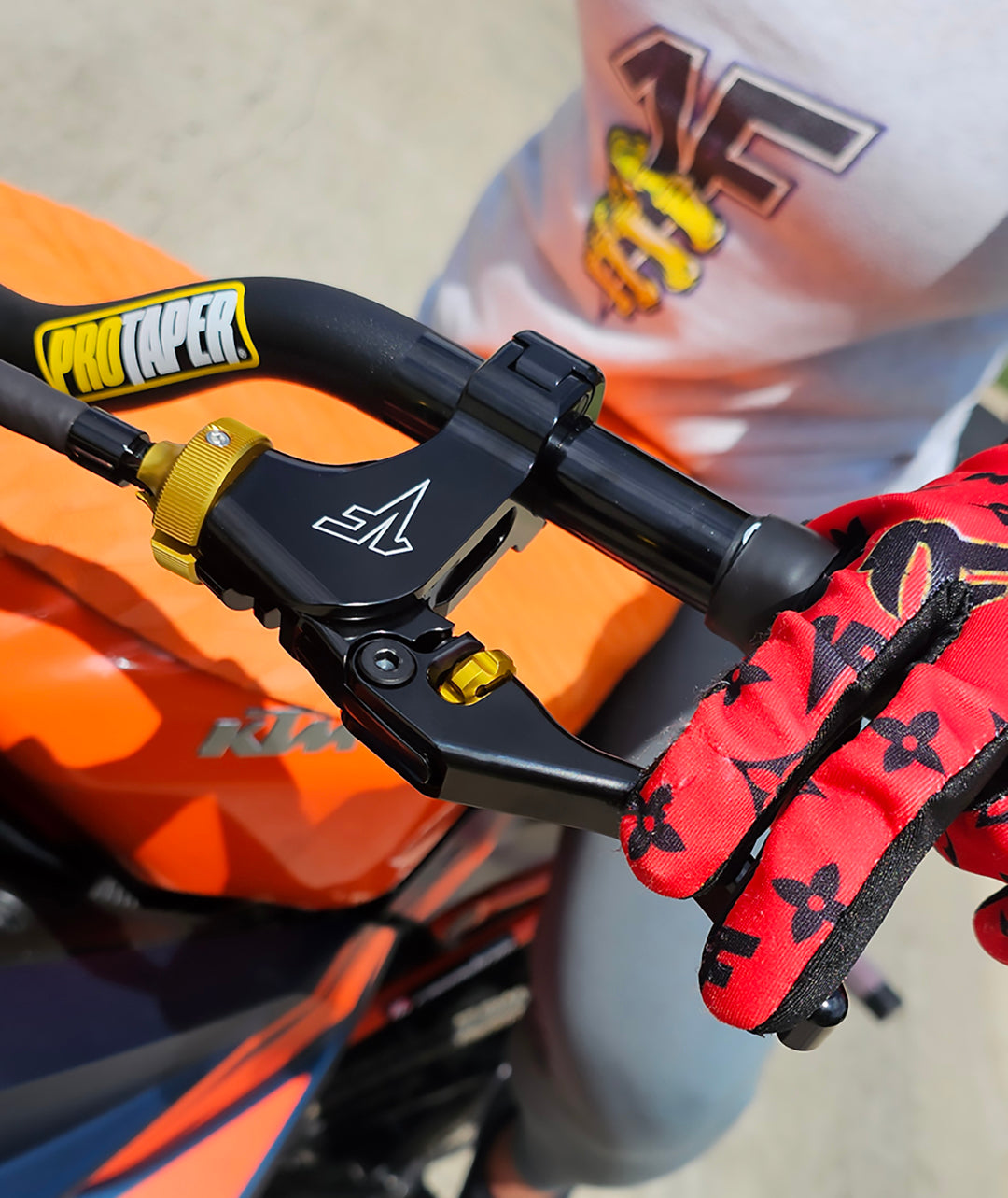 Close-up of a gloved hand holding 1FNGR quickie easy pull clutch adjustable lever with gold adjusters on handlebar